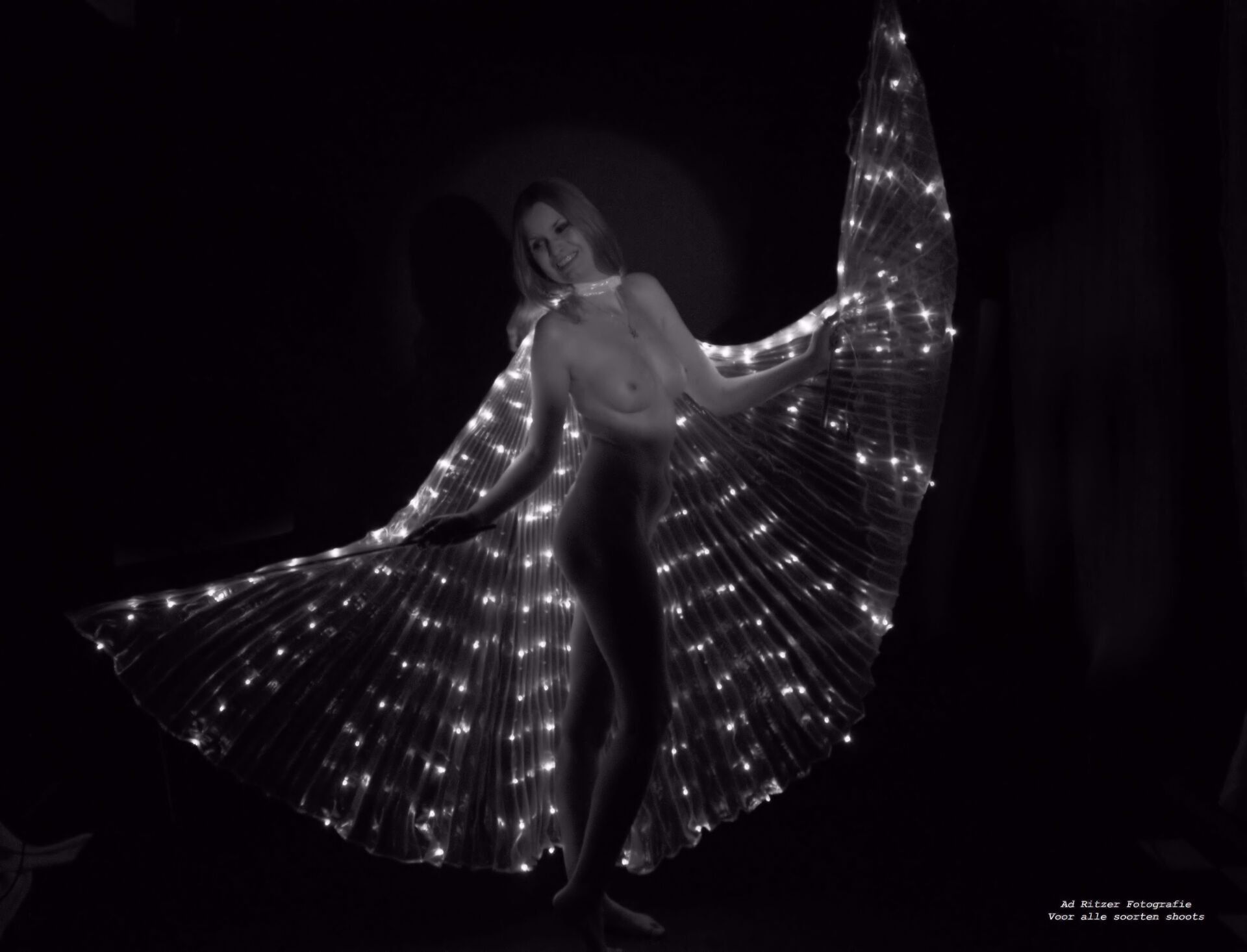 Vrouw poseert met een verlichte, vleugelachtige stof tegen een donkere achtergrond.