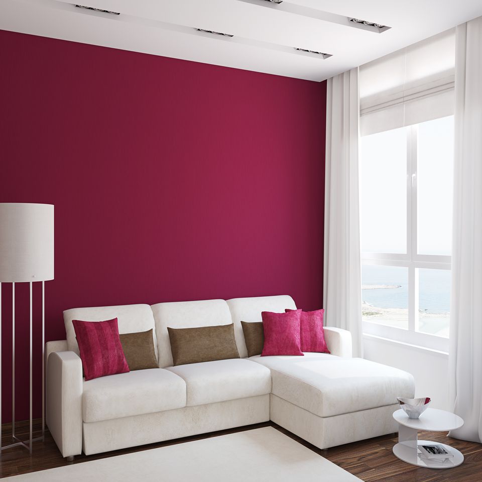 Soggiorno moderno con parete d'accento color magenta, divano componibile bianco, lampada da terra e ampia finestra.