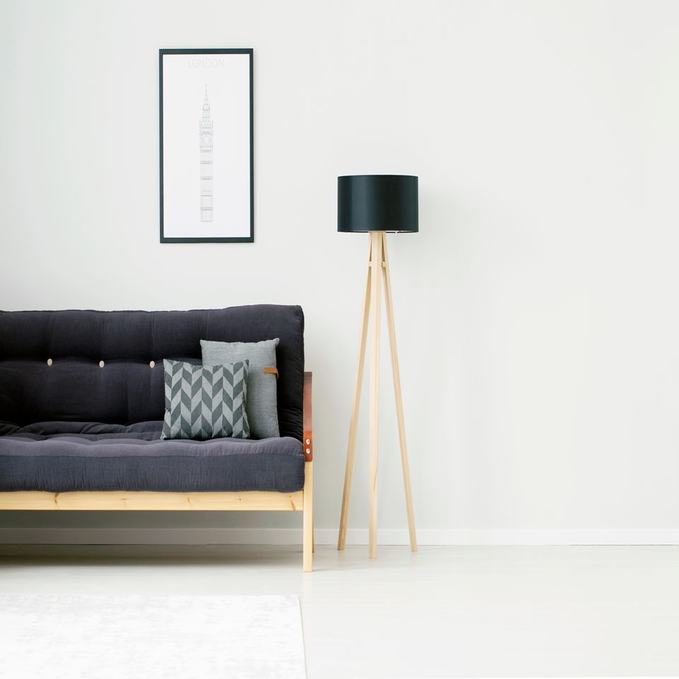 Soggiorno minimalista con divano scuro, quadri incorniciati alle pareti e lampada da terra nera su una parete bianca.