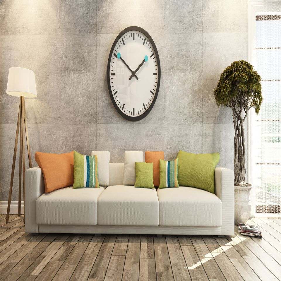 Luminoso soggiorno con divano bianco, cuscini colorati, orologio da parete, lampada da terra e pianta su pavimento in legno.