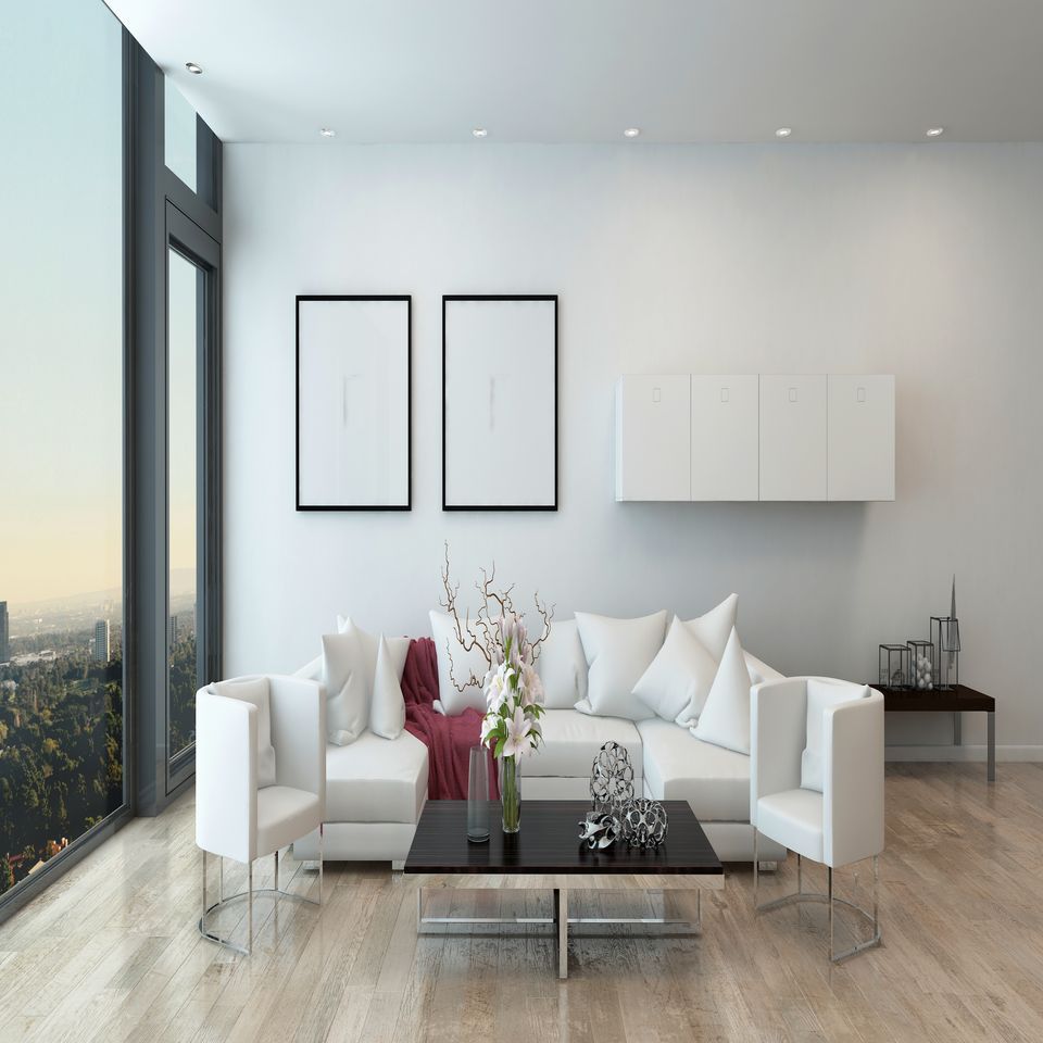 Soggiorno moderno e minimalista con mobili bianchi, tavolino da caffè in vetro, opere d'arte alle pareti e vista sulla città attraverso ampie finestre.