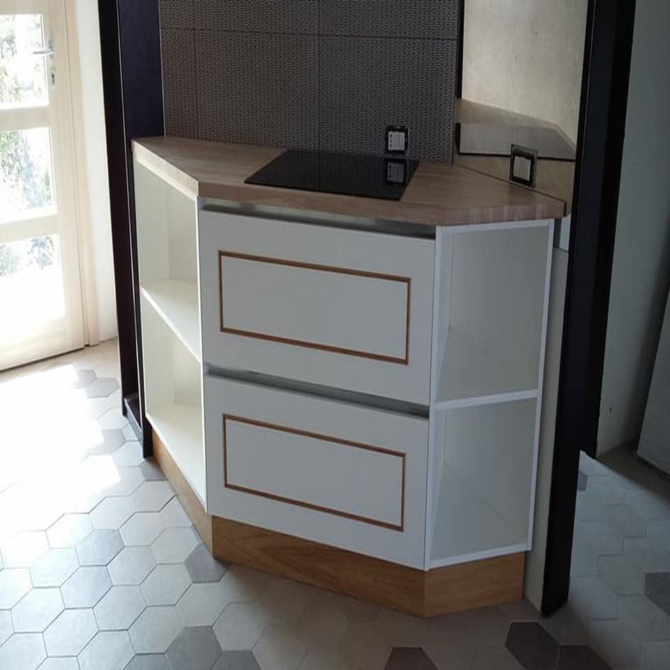 Mobile angolare bianco con finiture in legno e piano di lavoro scuro in una stanza piastrellata vicino a una porta