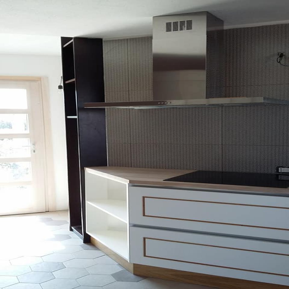 Cucina moderna vuota con paraschizzi in piastrelle grigie, cassetti bianchi, mensole nere e cappa aspirante centrale.