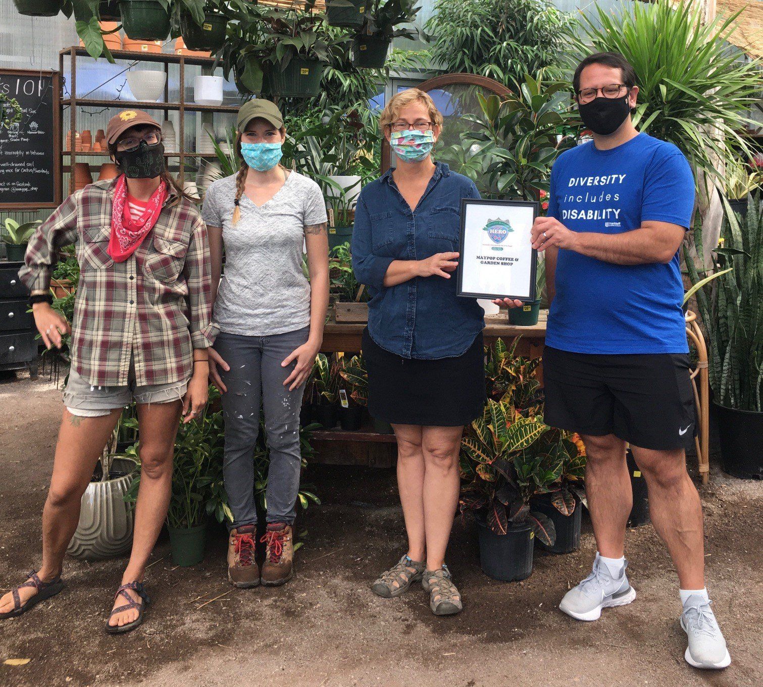 Four people wearing masks pose in a greenhouse, holding an award.