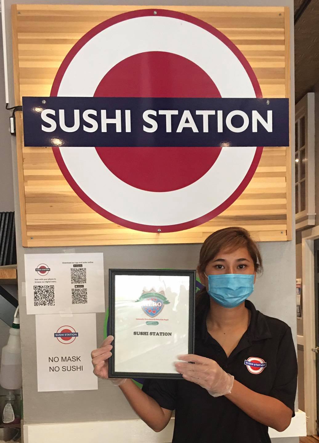 Woman in mask and gloves holds award at Sushi Station, logo with red and blue circles.