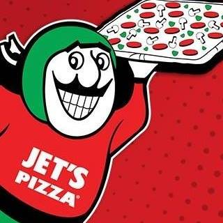 Jet's Pizza mascot holding a pizza, wearing a green helmet and red shirt on a red dotted background.