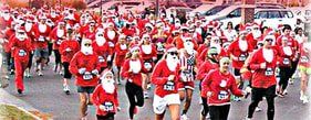 Large crowd of people in Santa Claus costumes running in a street race.