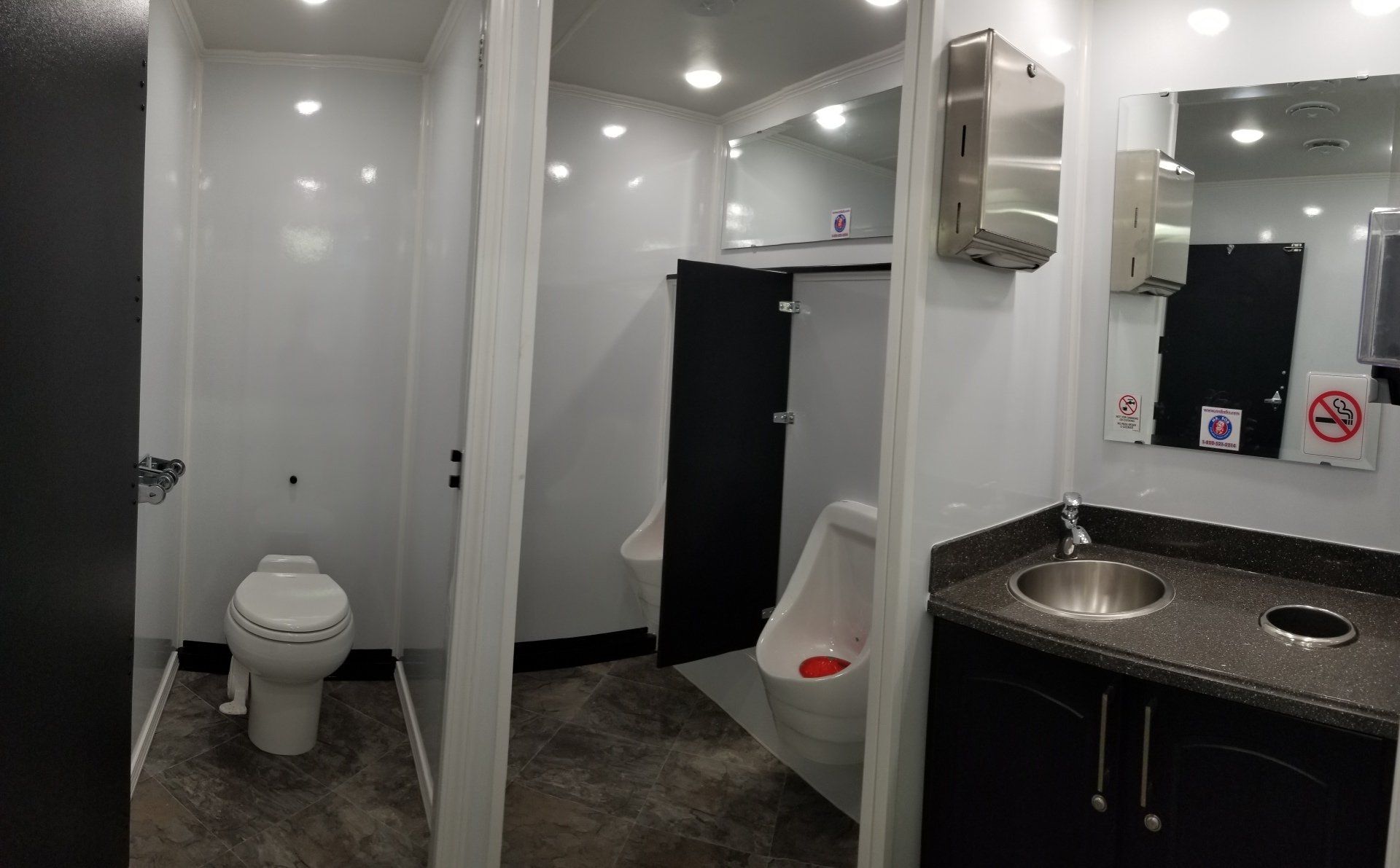 Interior of a portable restroom with white walls, a toilet, urinal, sink, and mirror.