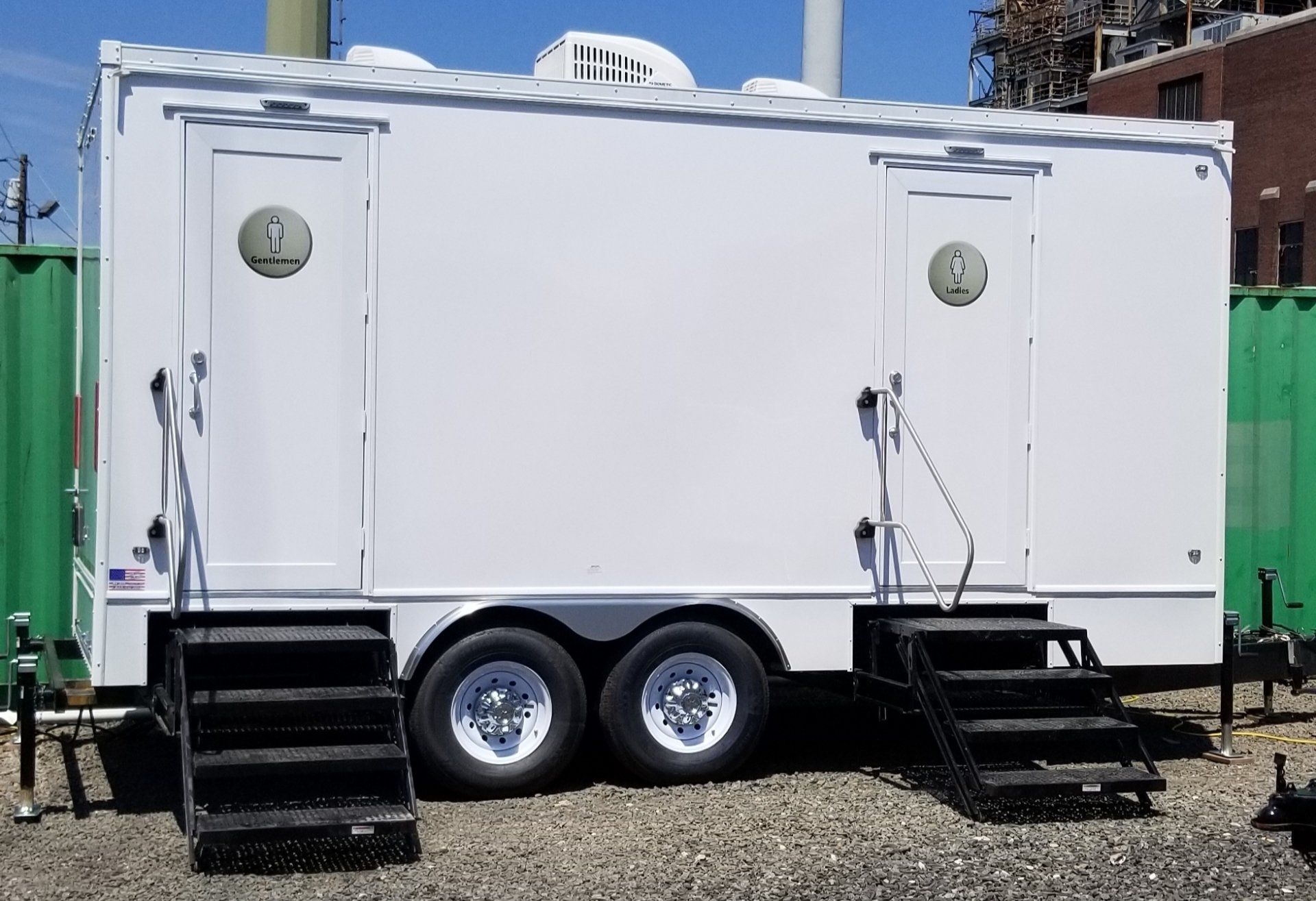 White portable restroom trailer with two separate entrances and black stairs.