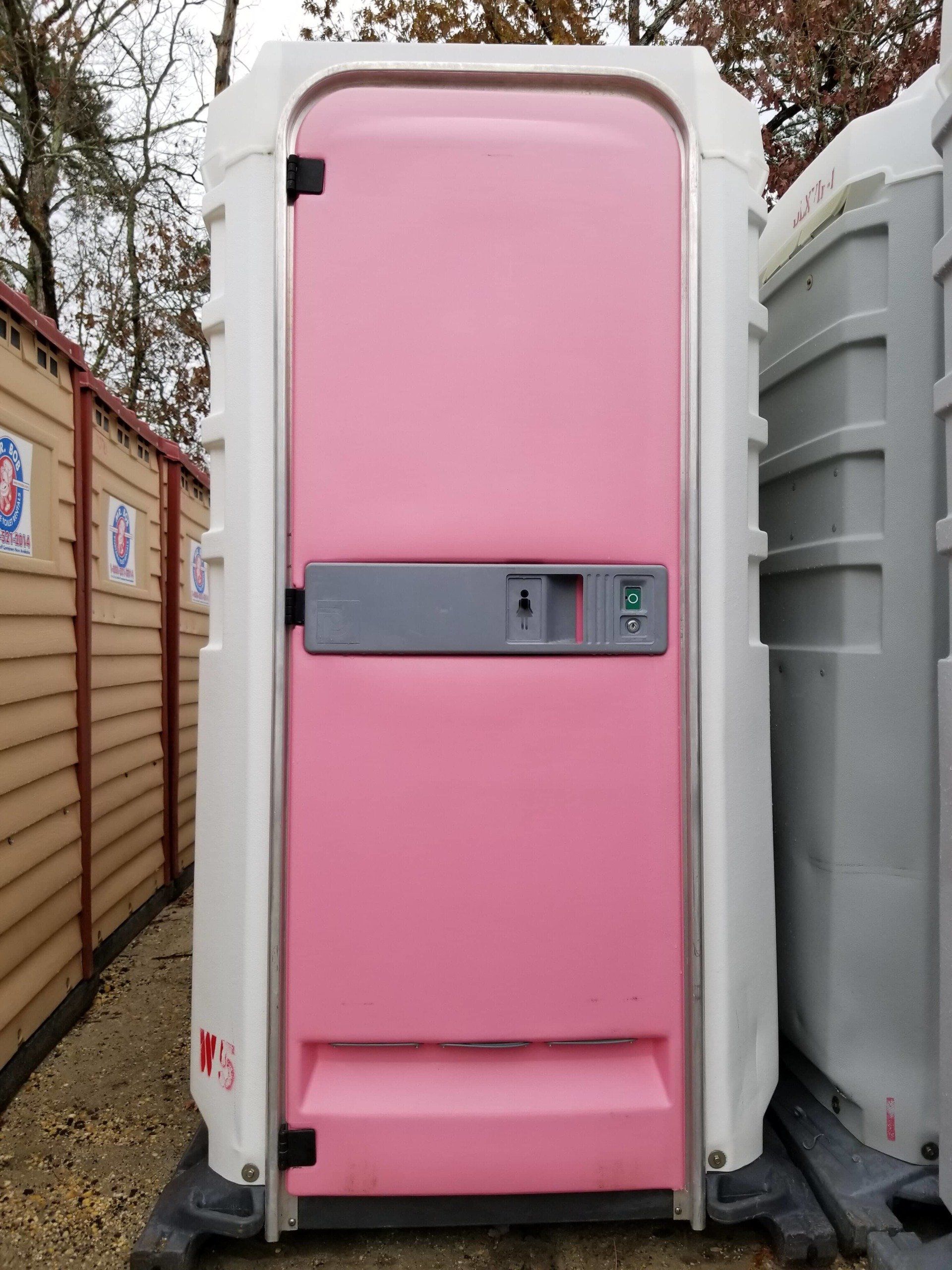 Pink portable toilet with white trim, outdoors.