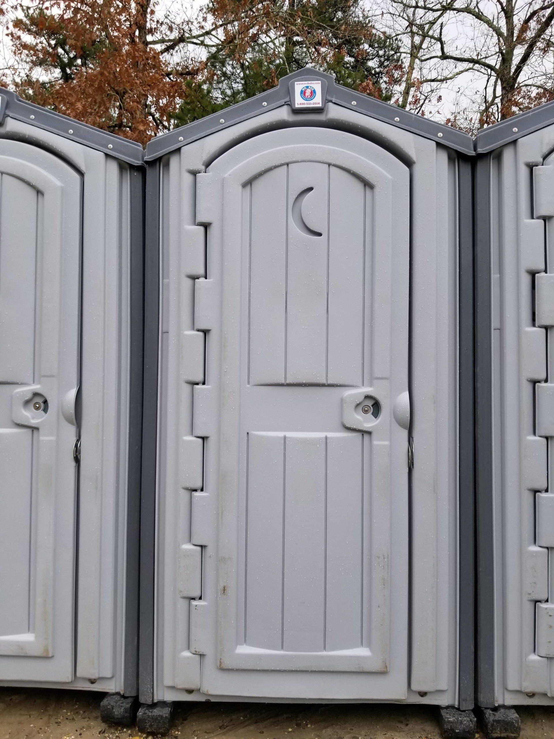 Three gray portable toilets, one with a crescent moon cutout on the door.