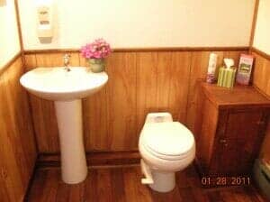 Small bathroom with a pedestal sink, toilet, and wooden cabinet; wooden paneling and flooring.