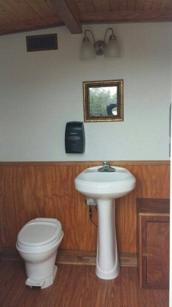 Small bathroom with toilet, pedestal sink, mirror, and paper towel dispenser.