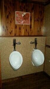 Two white urinals with metal fixtures mounted on a wood-paneled wall, in a public restroom.