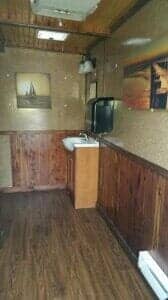 Interior of a small room with wood paneling, sink, and framed art. Dim lighting.
