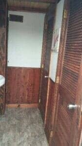 Narrow bathroom with wooden doors, walls, and flooring. A white wall and a sink are visible.