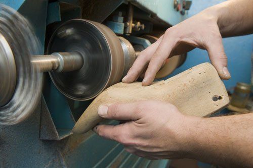 due mani con un pezzo di legno e accanto un disco di carta vetrata roteante per la levigatura