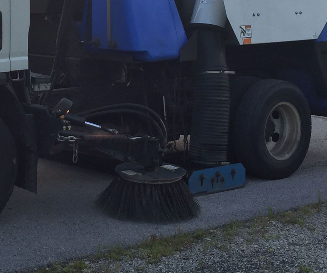 Parking Lot Sweeping Services. A power sweeper truck cleaning a concrete drive.