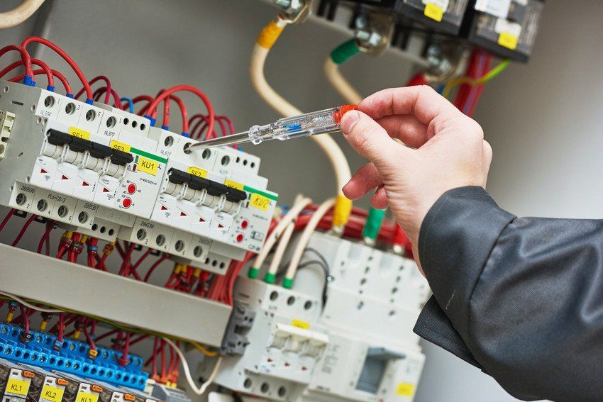 technician examining electric equipment with screwdriver meter tester in fuse box