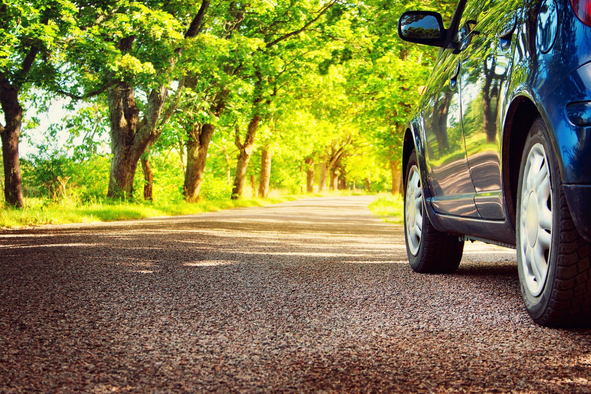 A blue car is parked on the side of a road surrounded by trees.