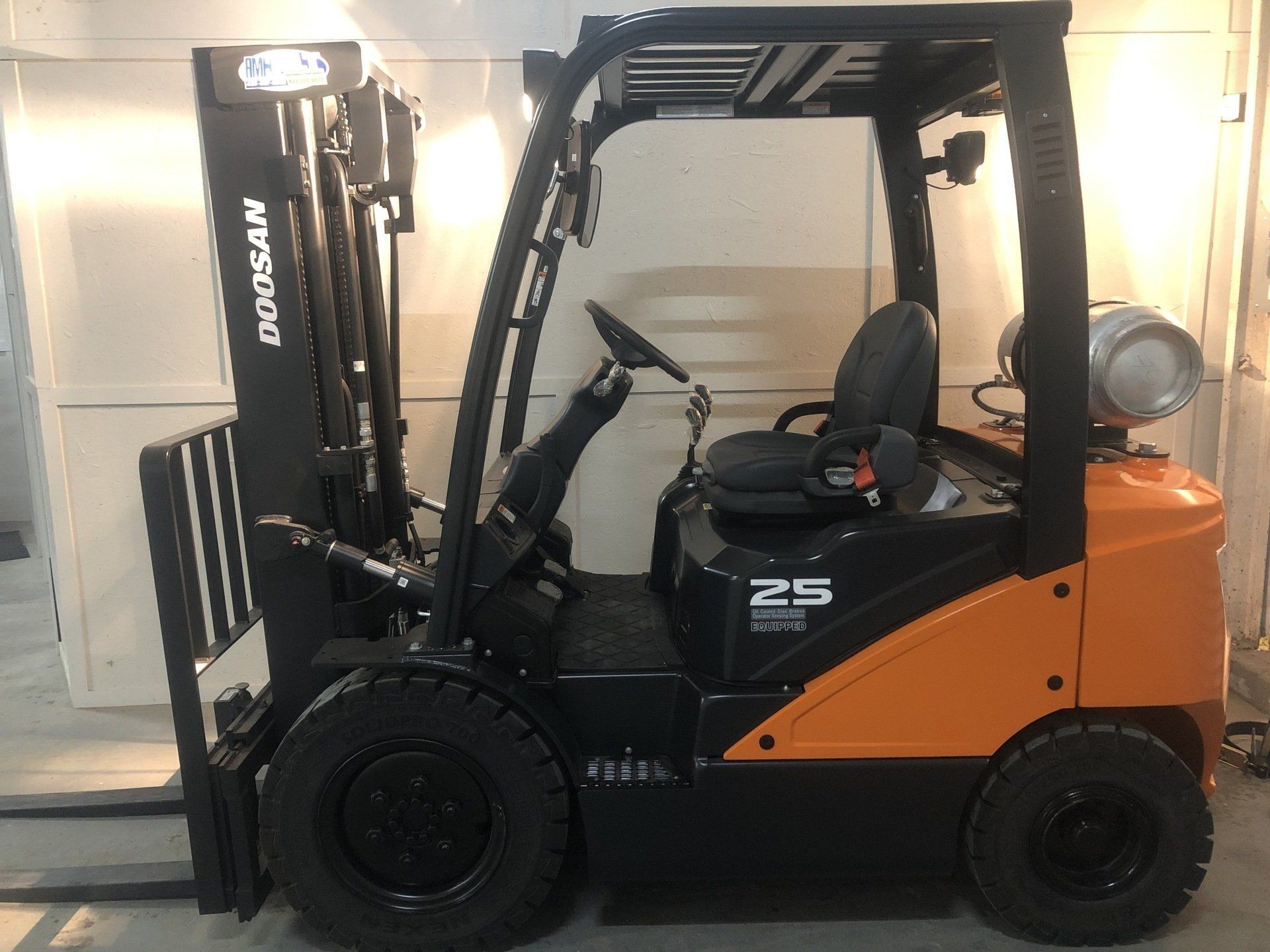 Orange and black forklift parked indoors beside white wall, side view
