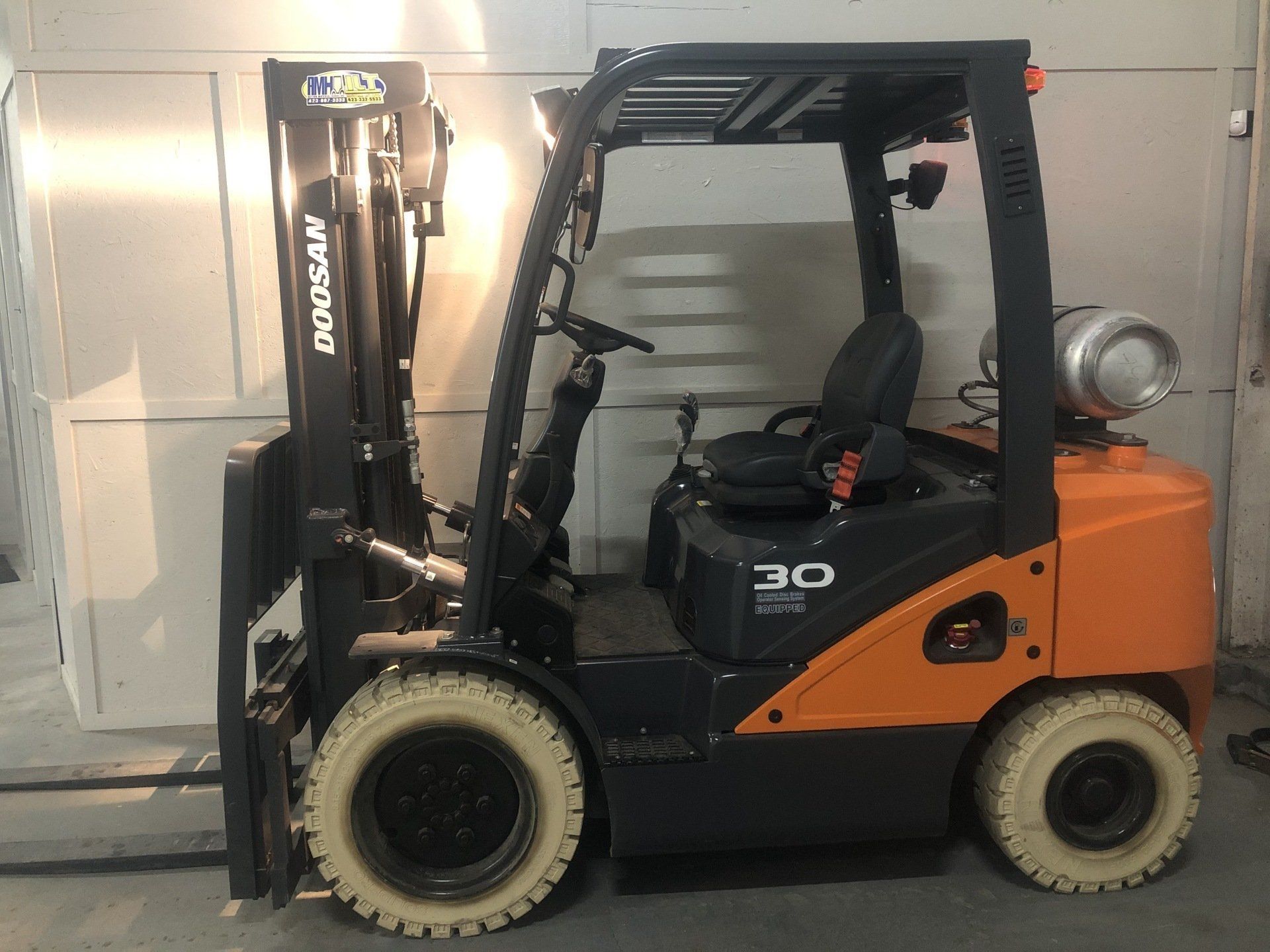 Orange and black forklift parked indoors beside a metal wall
