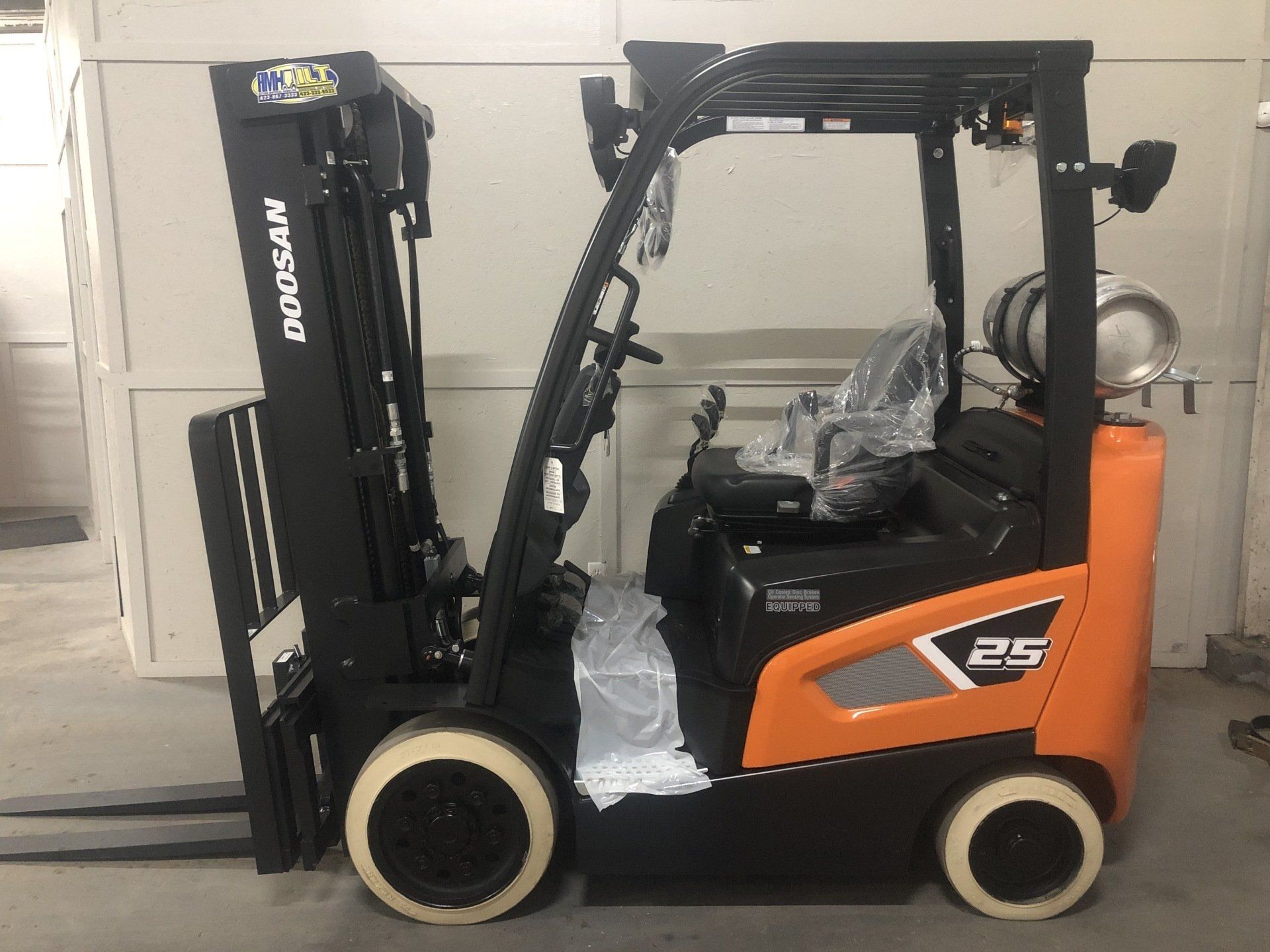 Orange and black forklift parked indoors beside a closed garage door