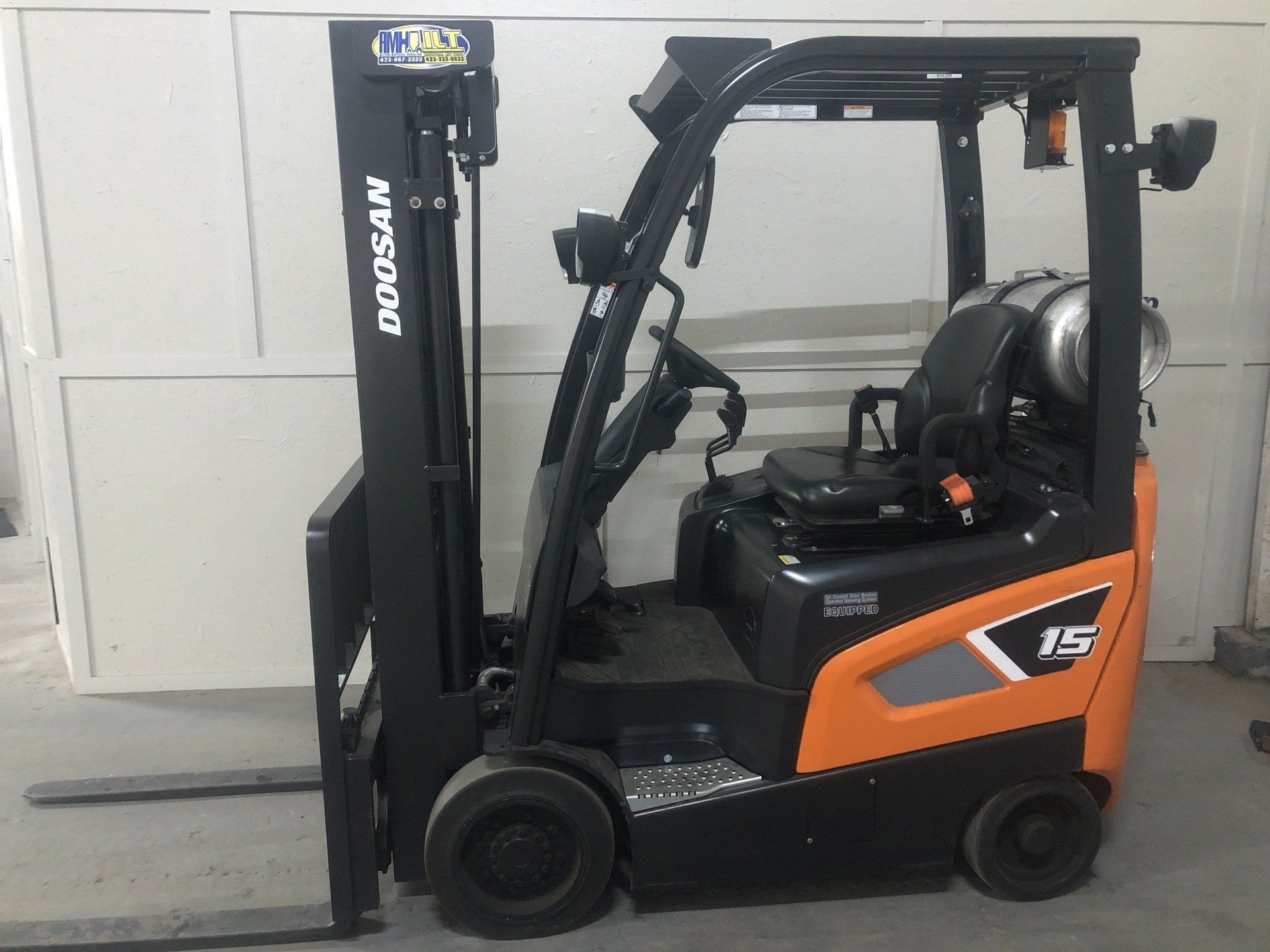Orange and black forklift parked indoors beside a closed white garage door
