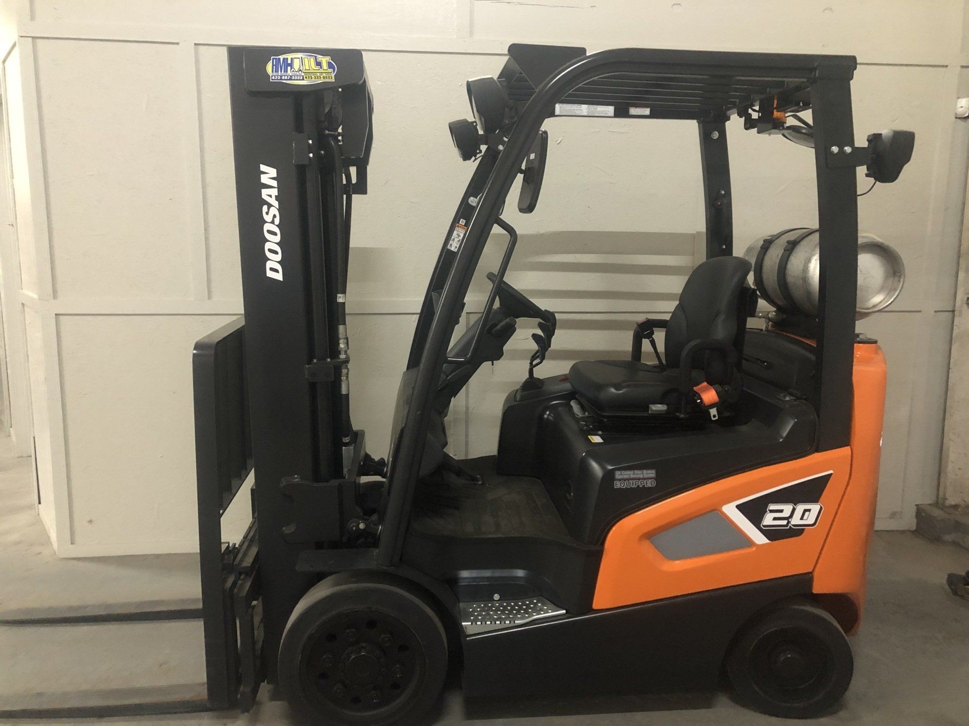Black and orange forklift parked indoors against a wall