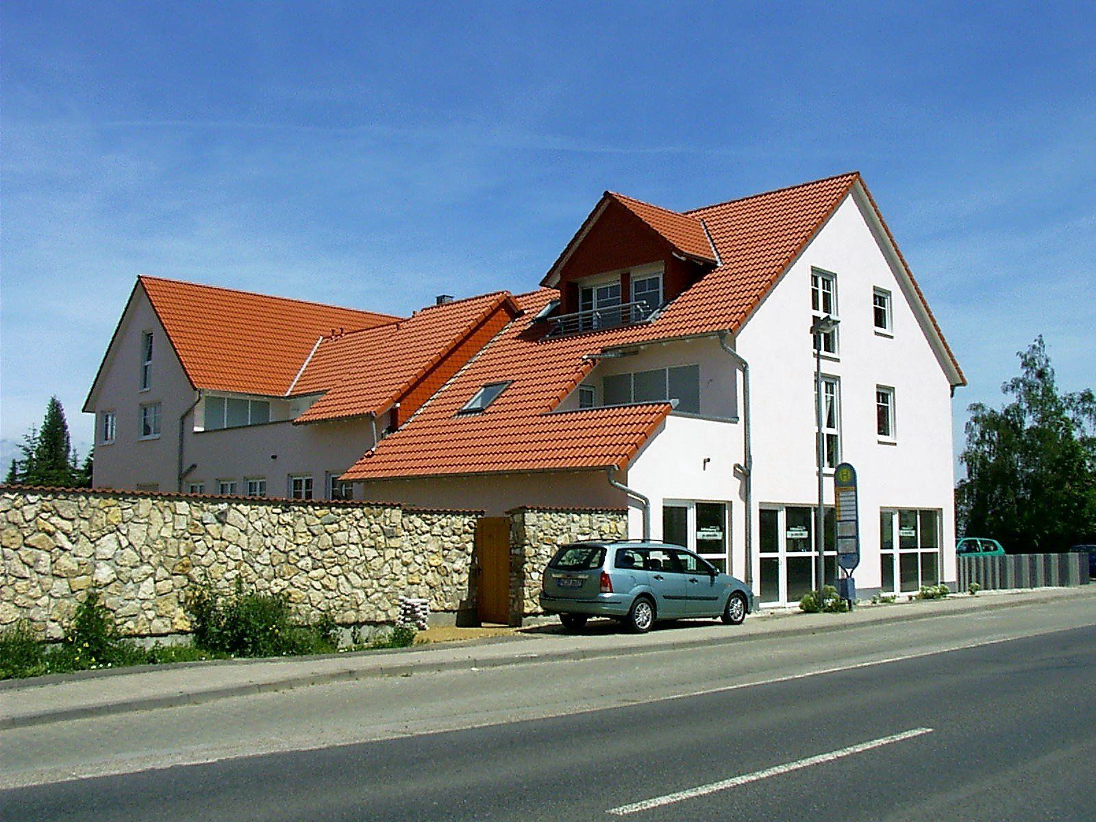 Ein weißes Haus mit einem roten Ziegeldach und einem davor geparkten blauen Auto