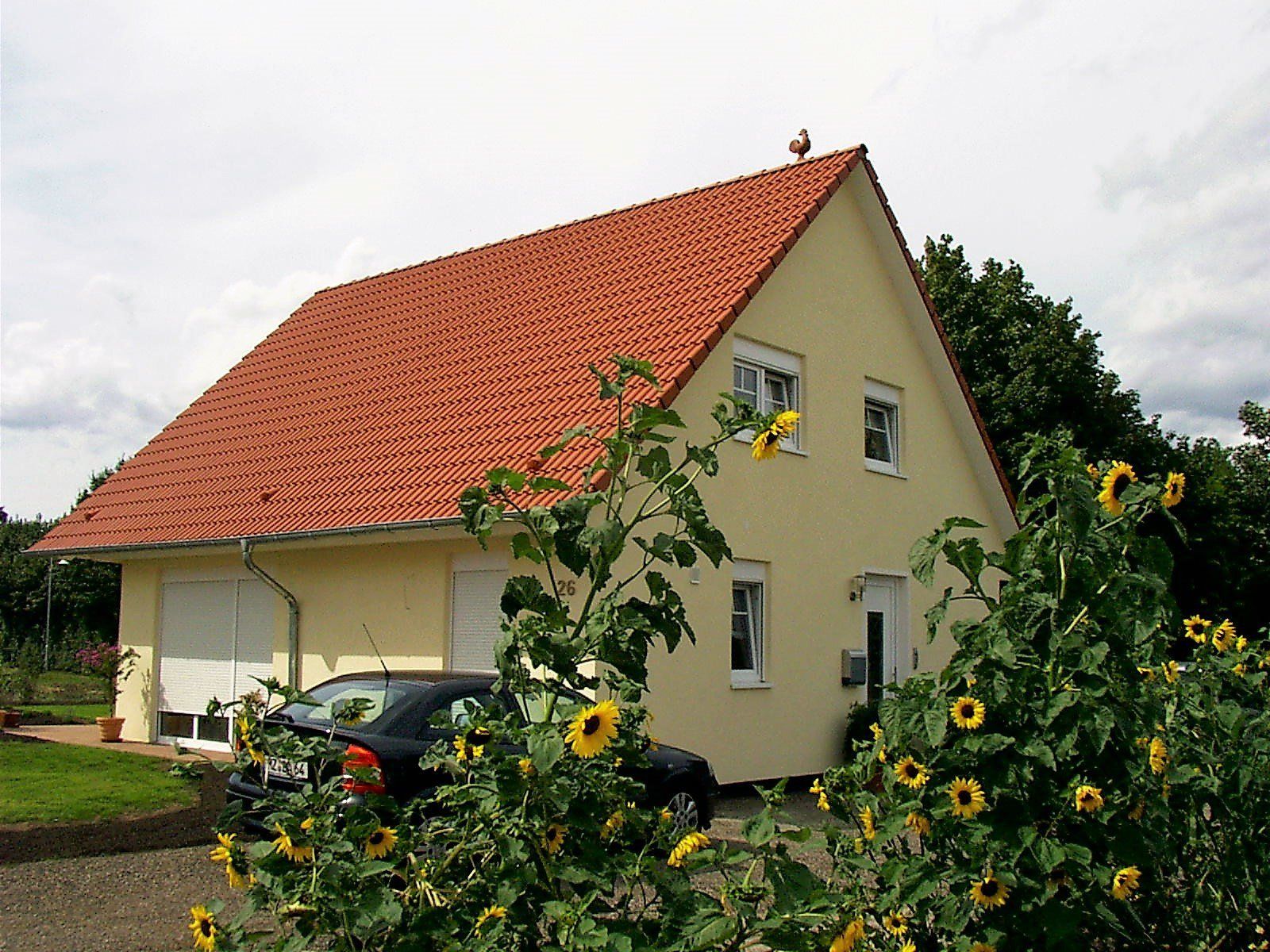 Ein Auto parkt vor einem gelben Haus mit rotem Dach
