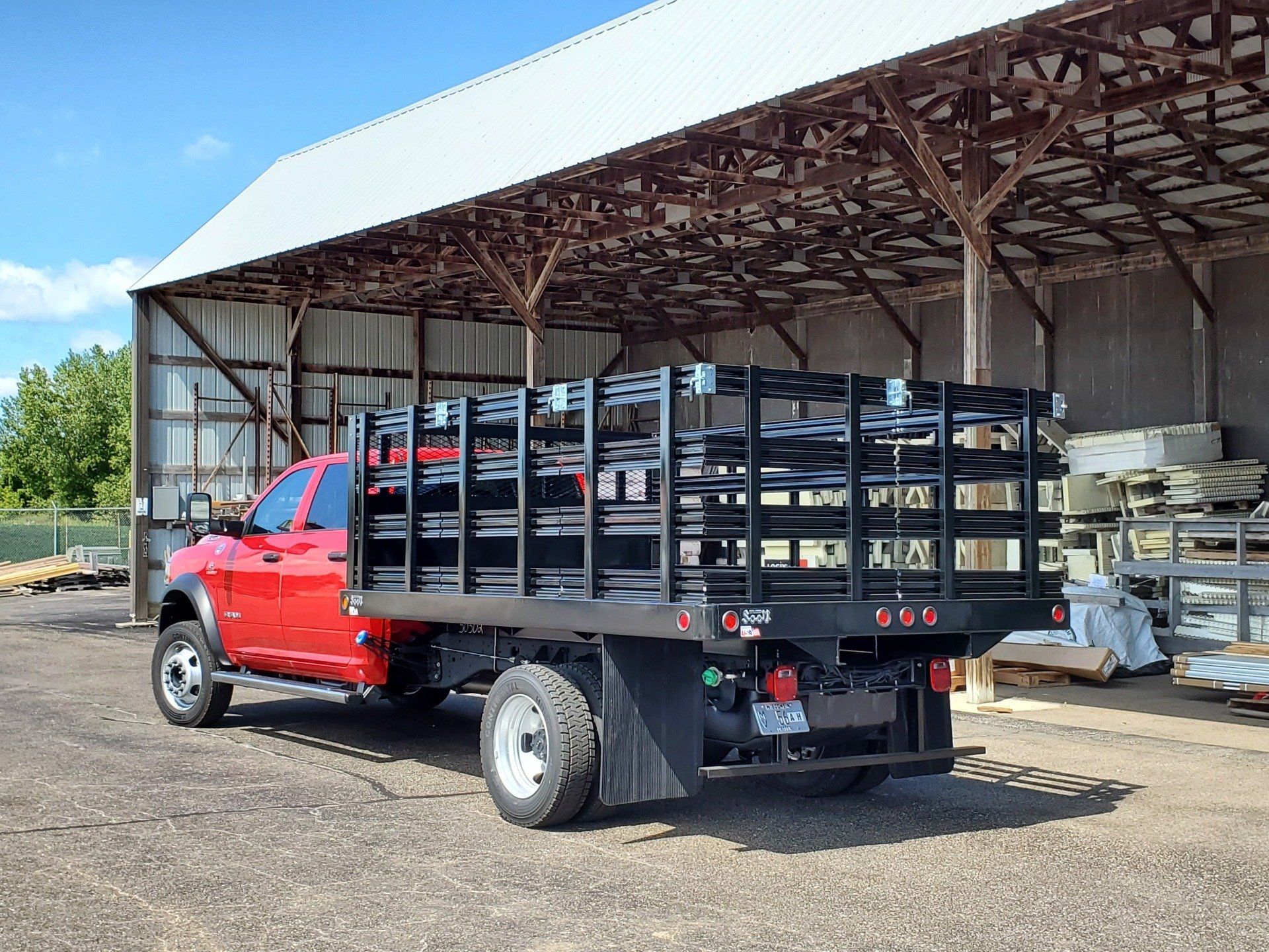 A red truck with a flat bed is parked in front of a barn.