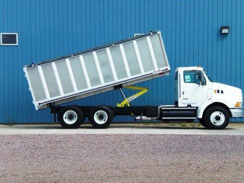 A white dump truck is parked in front of a blue building.