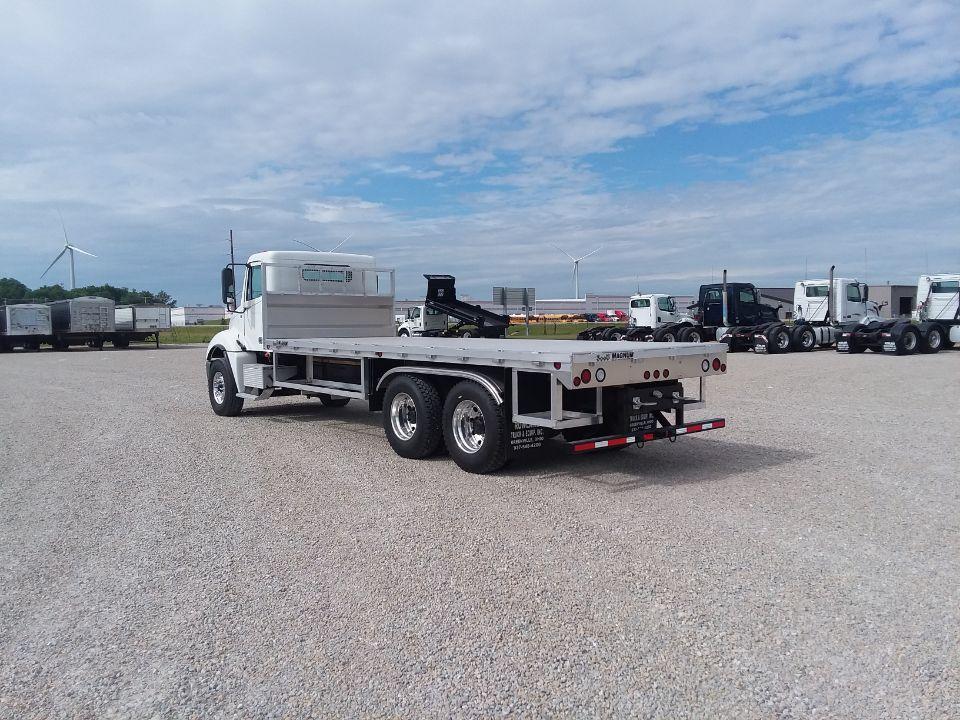 A flatbed truck is parked in a gravel lot.