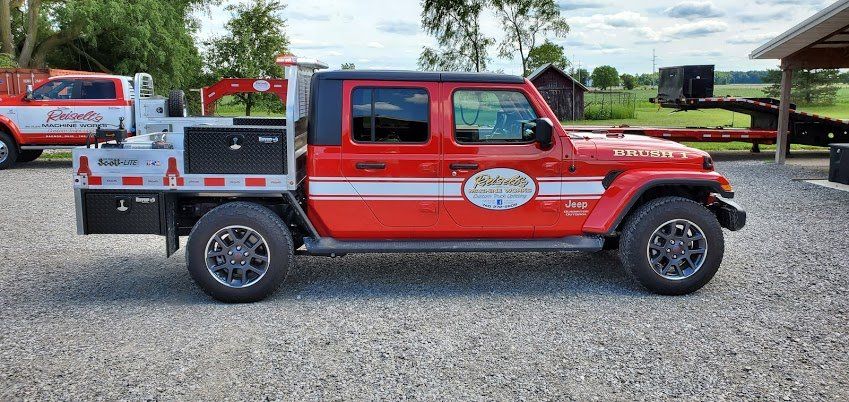 A red jeep is parked in a gravel lot next to a white truck.