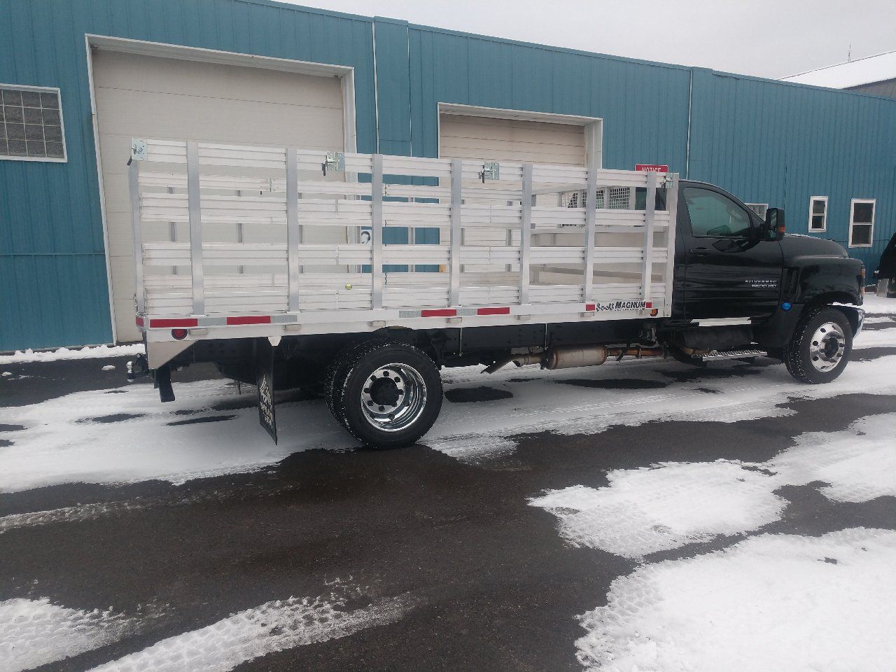 A truck with a wooden bed is parked in the snow in front of a building.