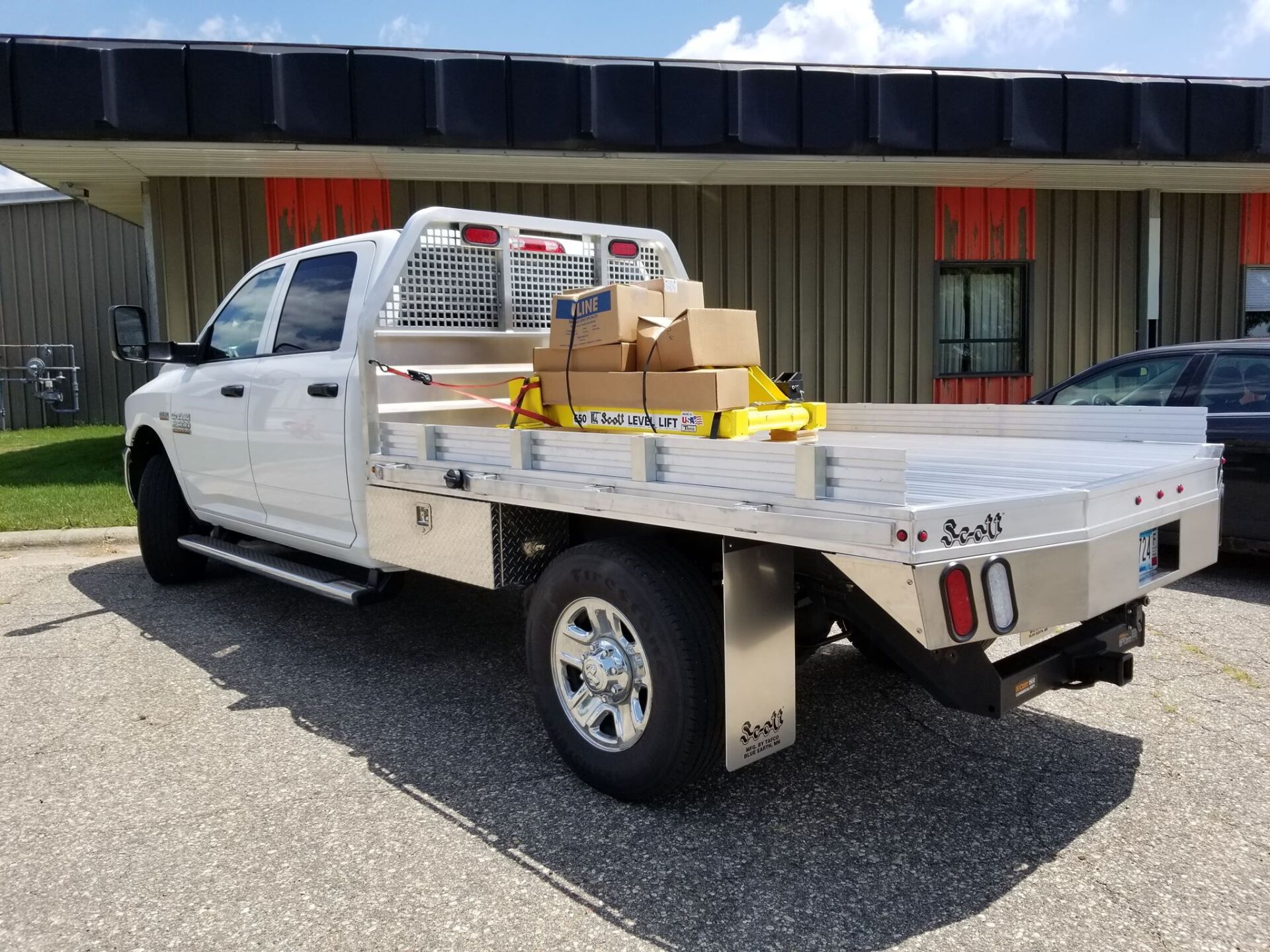 A white truck with a flat bed is parked in front of a building.