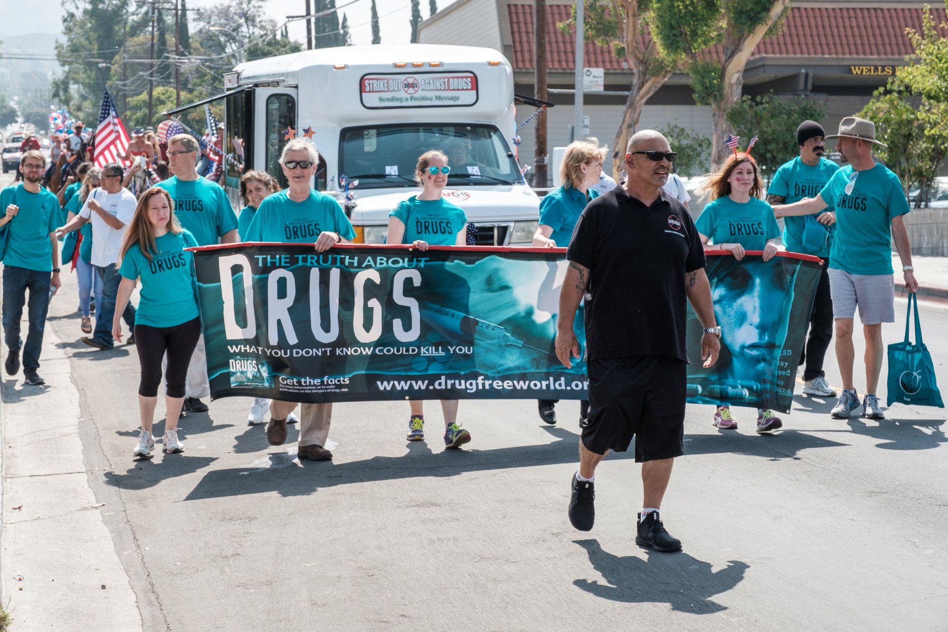 A group of people marching down a street holding a banner that says drugs