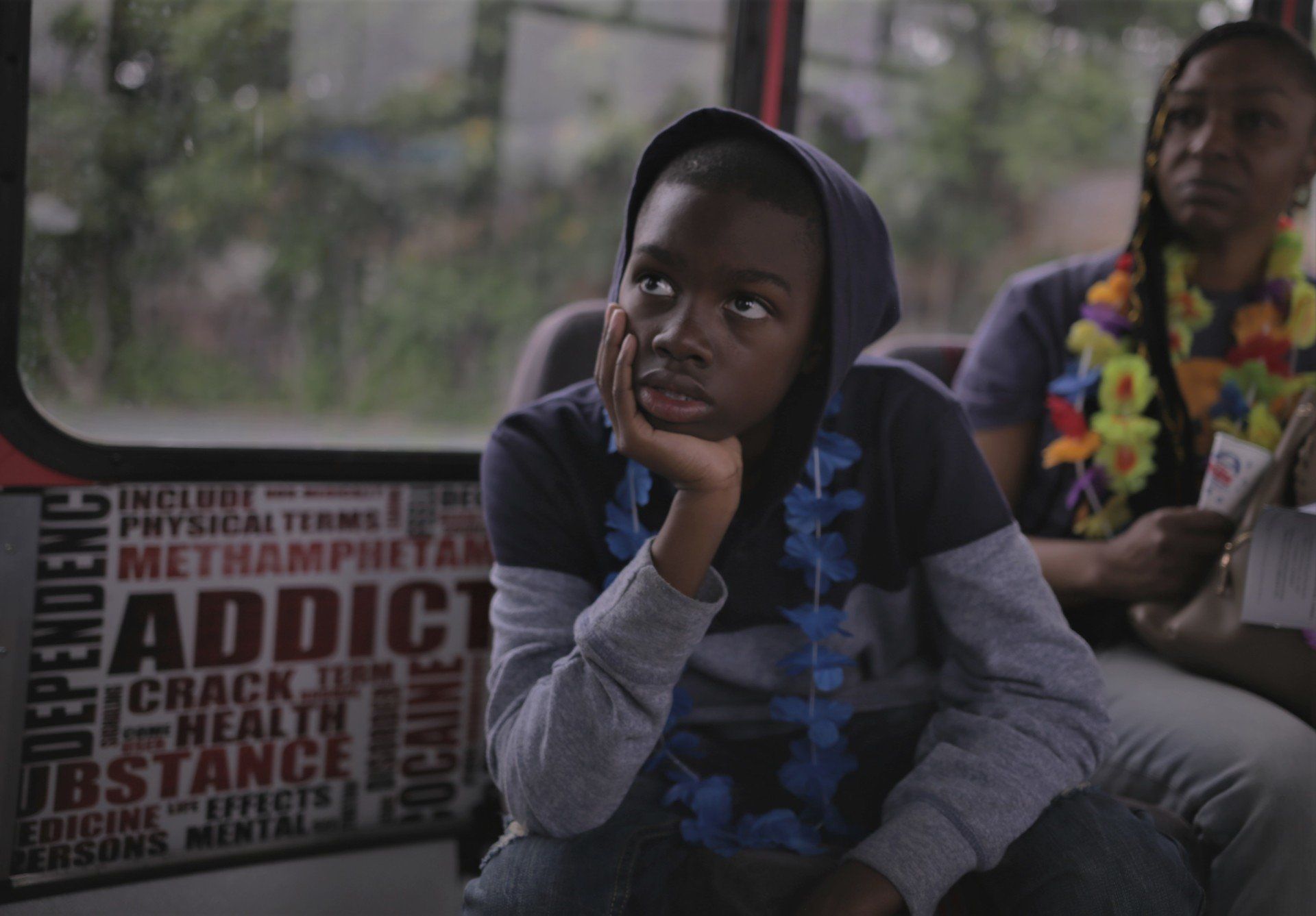 A boy is sitting on a bus with a sign that says addict