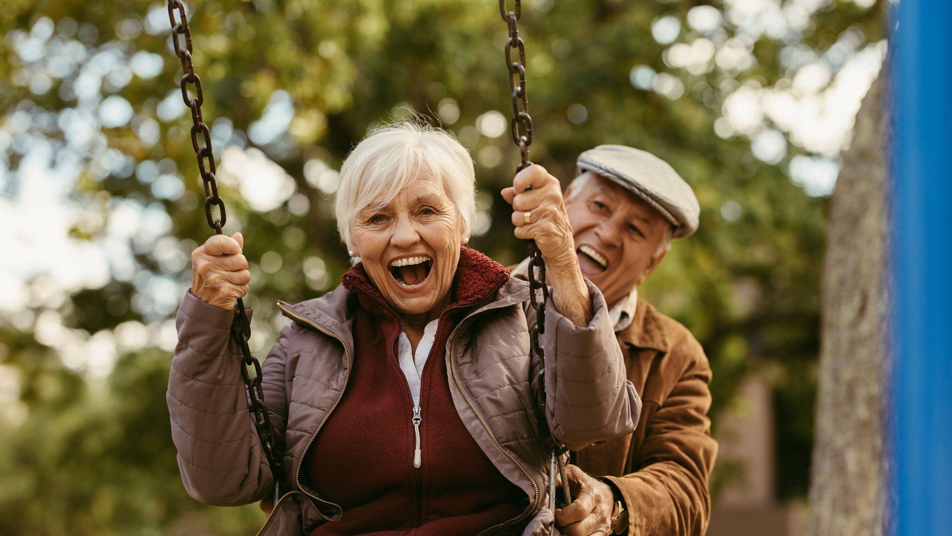 Elderly couple laughing, swinging on a playground swing.