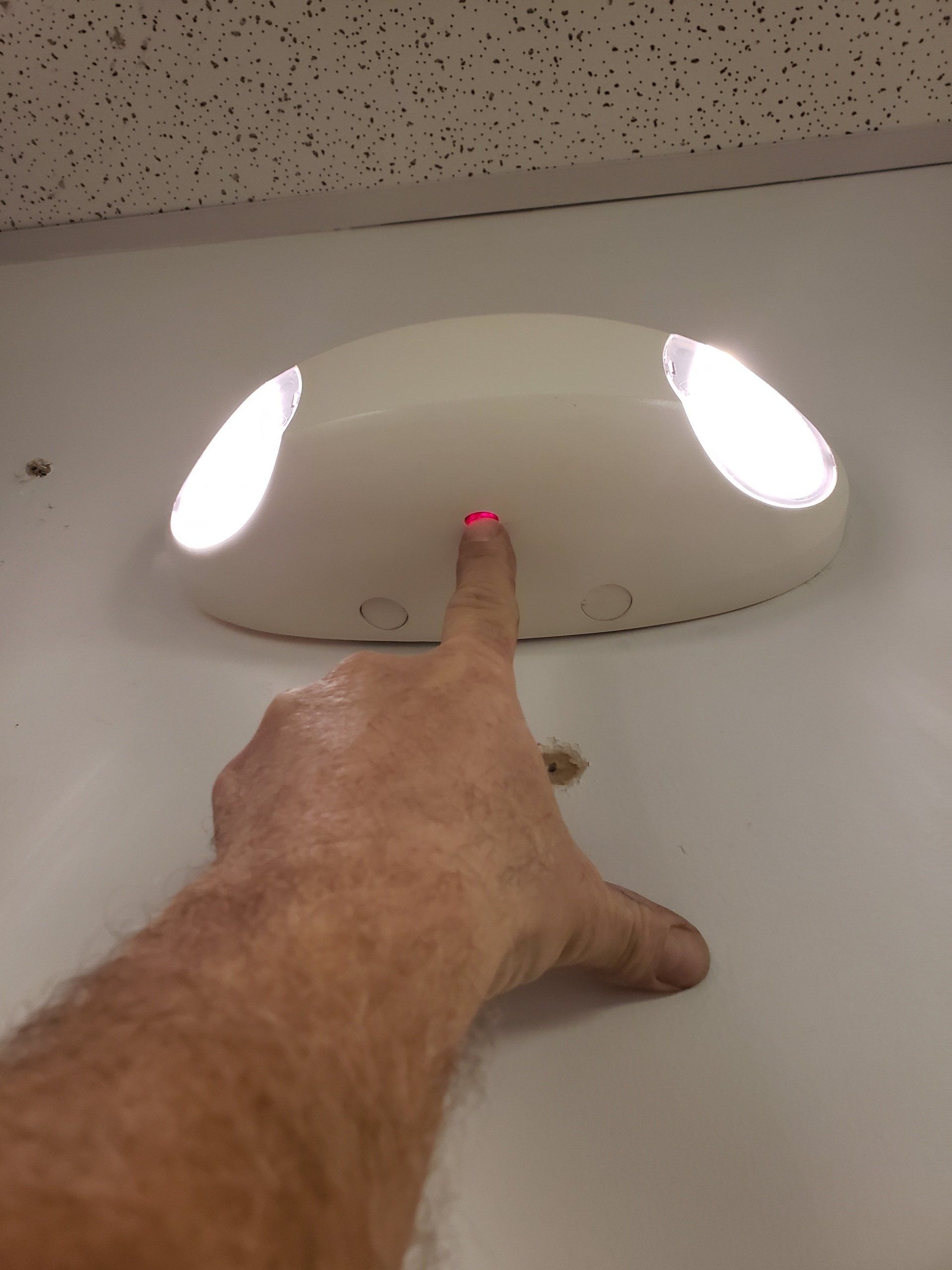 Finger pressing a red-lit ceiling light switch on a white fixture with two glowing lamps