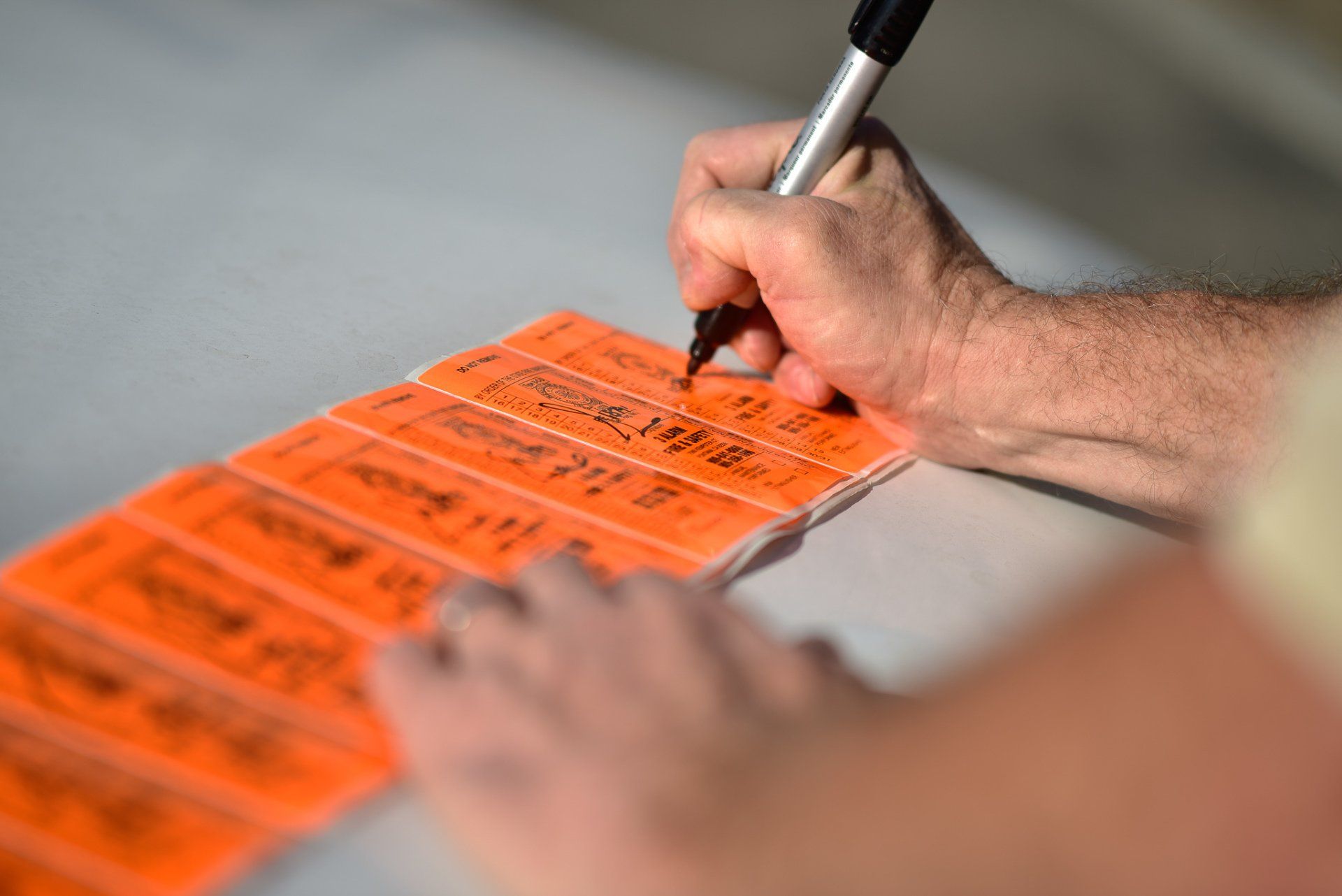Hand writing on orange ballot-style cards with a black pen on a table