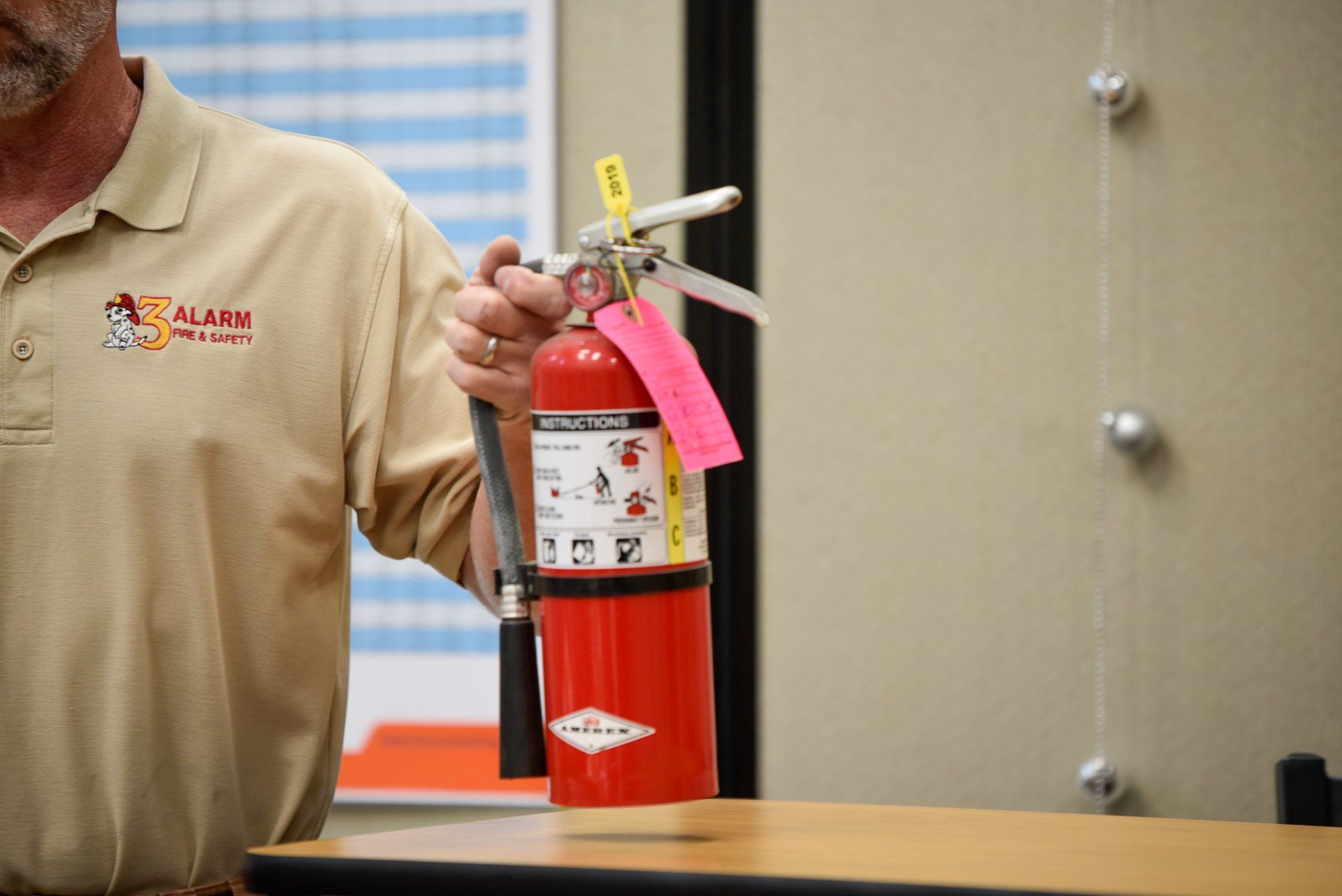 Person holding a red fire extinguisher with a pink tag in an indoor office setting