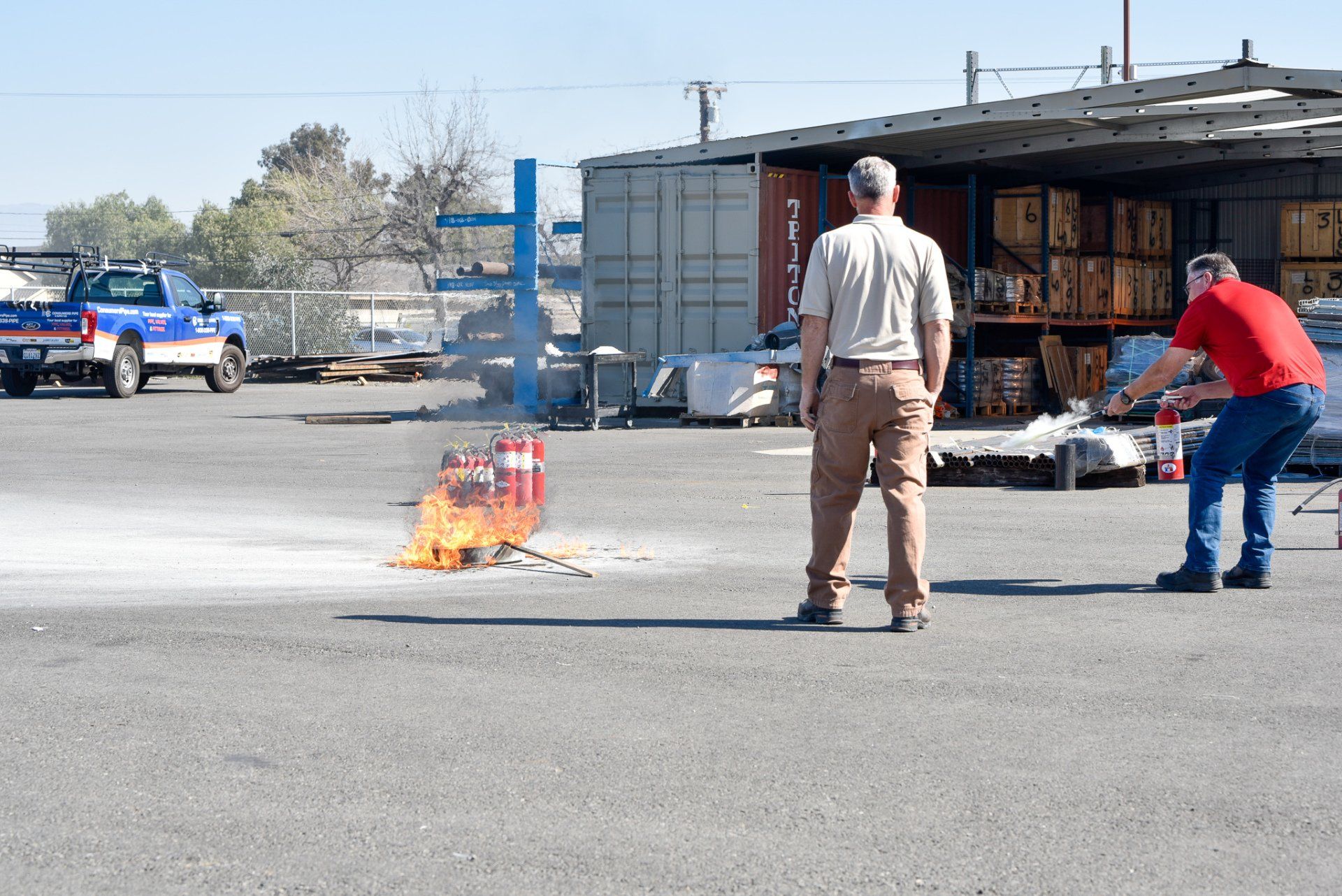 Two people near a small fire in a parking lot beside an open shipping container and truck.