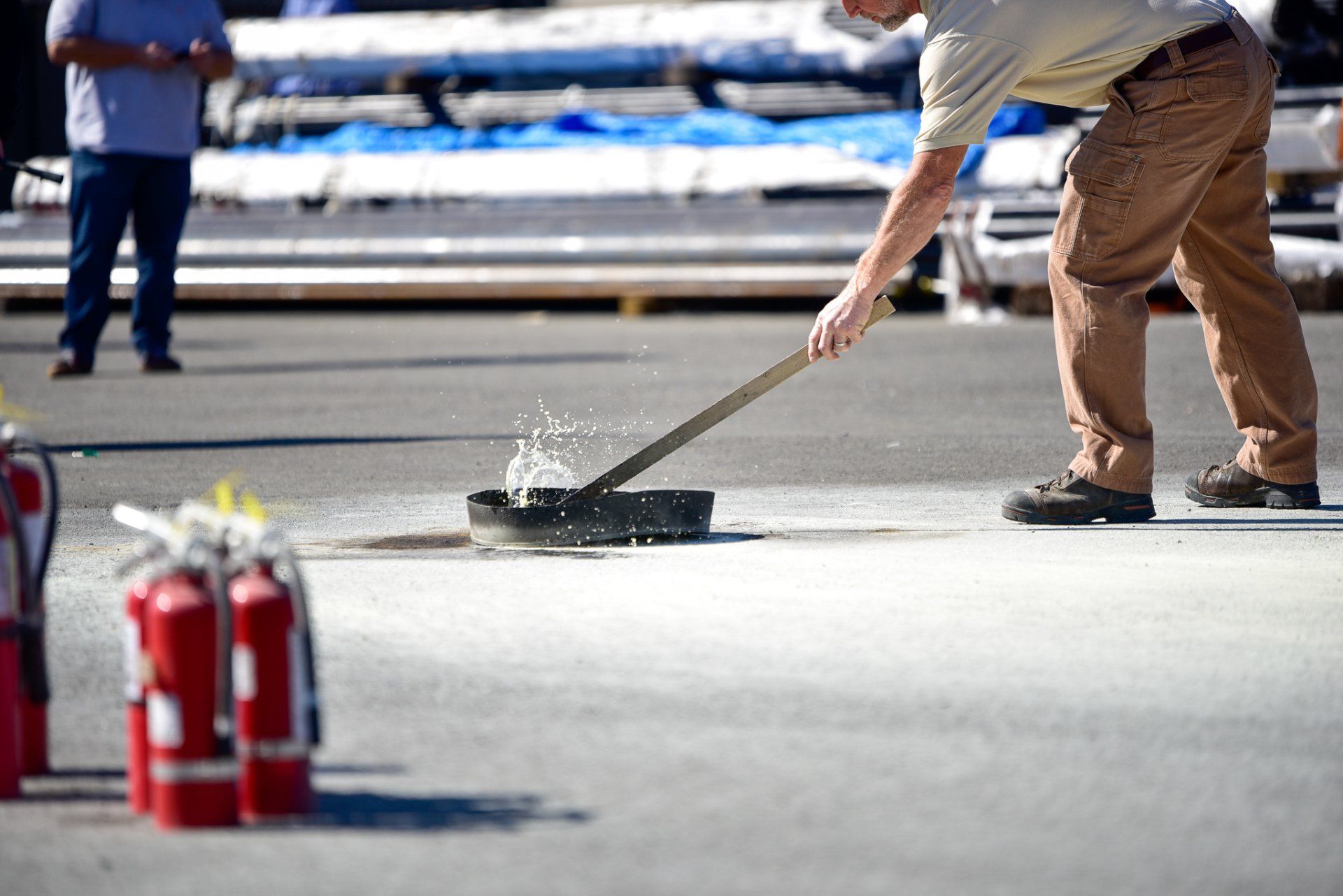 Worker using a long-handled squeegee on a wet pavement near fire extinguishers