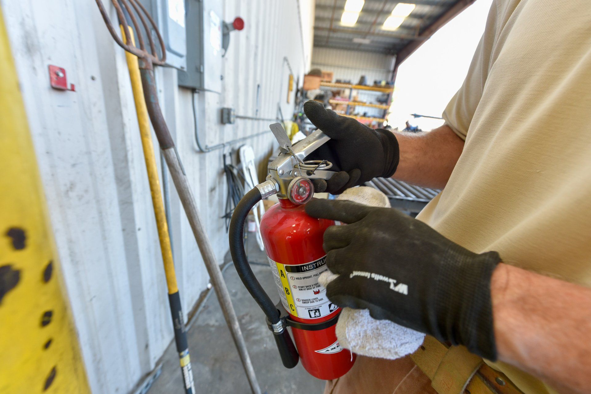 Technician’s gloved hands inspect a red fire extinguisher in a workshop or industrial hallway