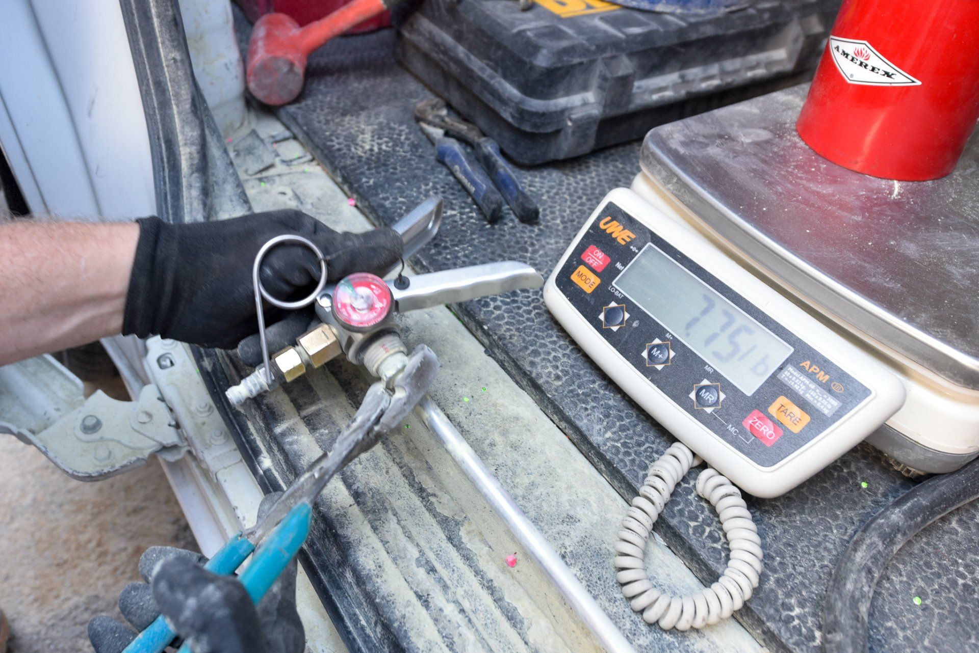Hand using a digital caliper on a metal part beside a digital scale in a workshop
