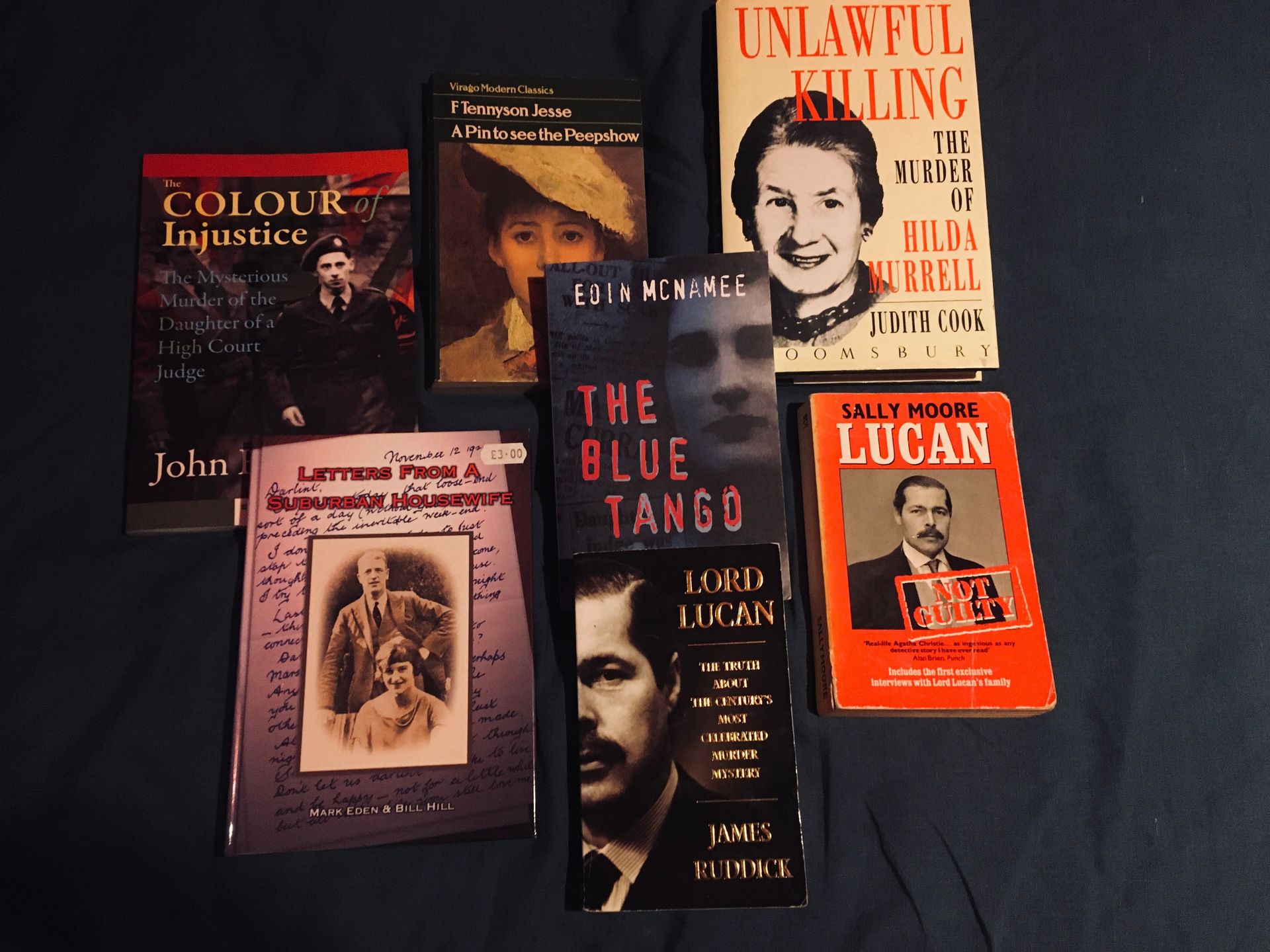 Seven books about true crime and historical figures arranged on a dark surface.