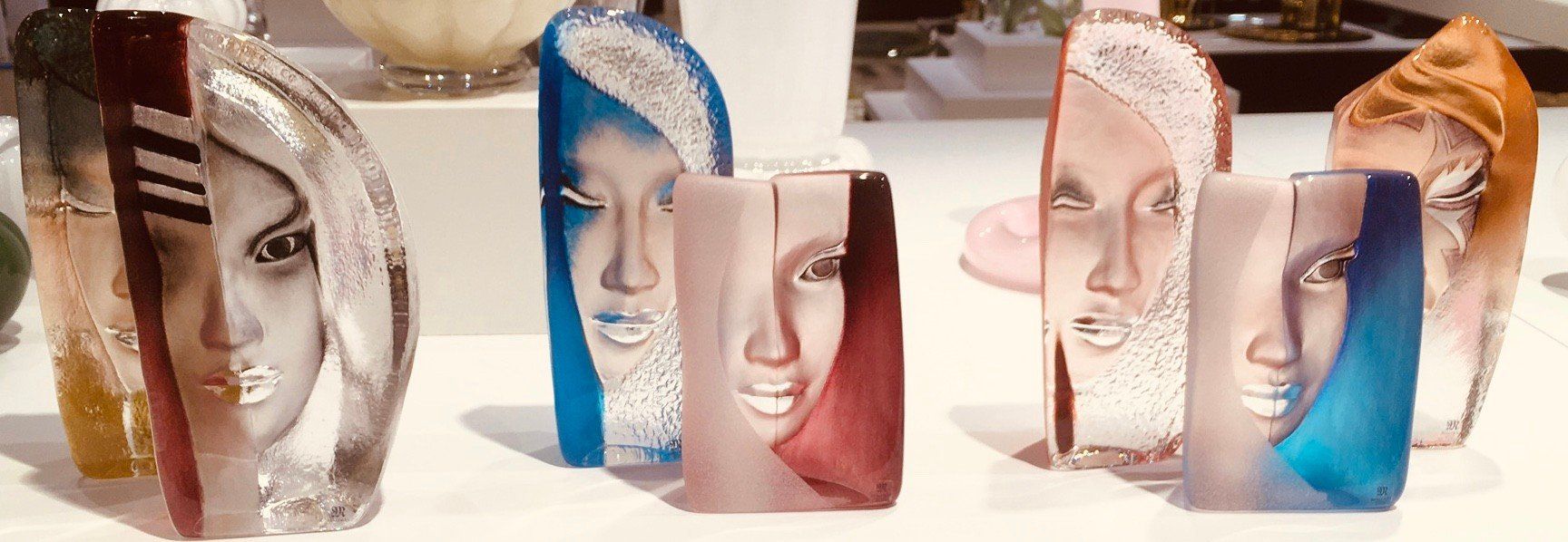 A row of stylized glass sculptures featuring abstract, colorful facial features on a white display surface.