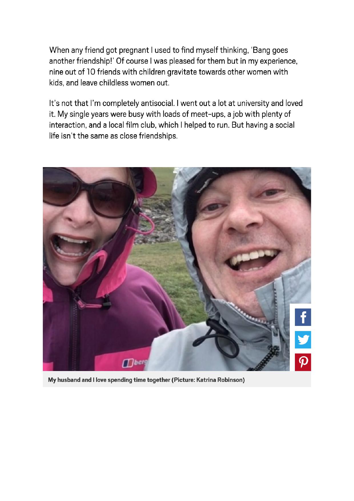 A smiling couple in waterproof outdoor gear poses for a selfie against a blurred natural background.